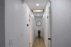 Hall with a textured wall, light wood-style flooring, and recessed lighting