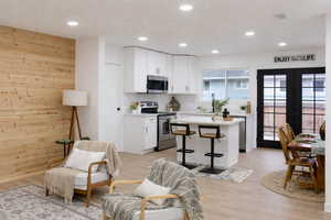 Kitchen with appliances with stainless steel finishes, white cabinetry, wood walls, a kitchen breakfast bar, and french doors