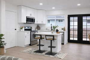 Kitchen featuring stainless steel appliances, white cabinets, a kitchen breakfast bar, light wood-style flooring, and french doors