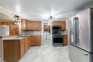 Kitchen featuring stainless steel appliances, brown cabinetry, a textured ceiling, and hanging light fixtures