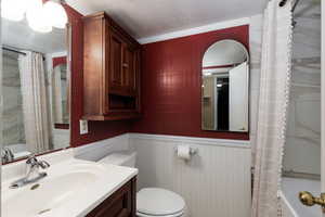 Bathroom with shower / tub combo, wainscoting, a textured ceiling, vanity, and ornamental molding