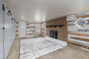 Living area with a textured ceiling, a brick fireplace, light carpet, and wood walls