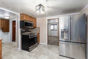Kitchen with stainless steel appliances, brown cabinets, a textured ceiling, light countertops, and ornamental molding