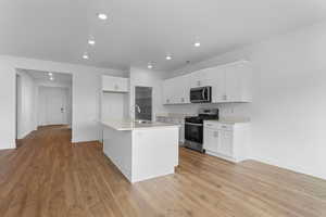 Kitchen featuring white cabinetry, stainless steel appliances, an island with sink, light wood-style floors, and recessed lighting