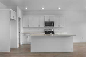 Kitchen featuring white cabinetry, appliances with stainless steel finishes, dark wood-style flooring, an island with sink, and recessed lighting
