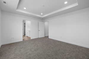 Unfurnished bedroom featuring a raised ceiling, carpet floors, recessed lighting, and ensuite bathroom