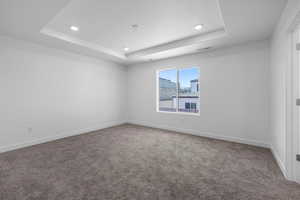 Empty room with a raised ceiling, carpet floors, and recessed lighting