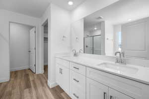 Full bathroom with a shower stall, double vanity, light wood-style floors, and a walk in closet