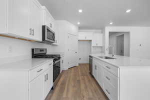 Kitchen with appliances with stainless steel finishes, white cabinets, a center island with sink, recessed lighting, and light stone counters