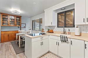 Kitchen with backsplash, light countertops, glass insert cabinets, white cabinets, and light wood-style floors