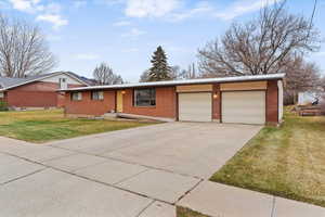 Ranch-style house with a front lawn, concrete driveway, brick siding, and a metal roof