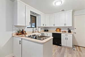 Kitchen featuring black appliances, light countertops, white cabinets, and light wood-style floors