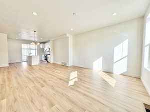 Unfurnished living room featuring a textured ceiling, light wood finished floors, recessed lighting, and a chandelier