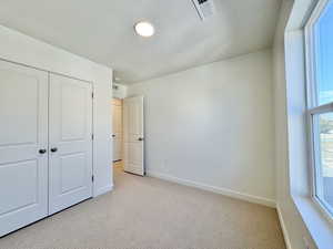 Unfurnished bedroom featuring light colored carpet, a textured ceiling, and a closet