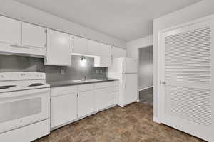 Kitchen featuring white appliances, white cabinetry, under cabinet range hood, backsplash, and stone finish flooring