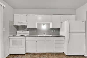 Kitchen featuring white appliances, white cabinets, under cabinet range hood, backsplash, and stone finish flooring