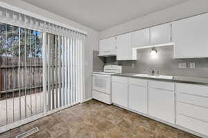 Kitchen with electric range, white cabinets, backsplash, under cabinet range hood, and stone finish floors