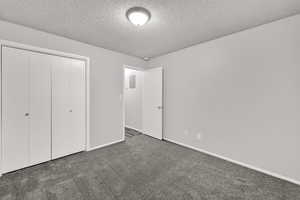 Unfurnished bedroom featuring carpet floors, a textured ceiling, and a closet