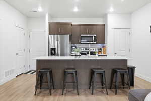 Kitchen with appliances with stainless steel finishes, dark brown cabinetry, a kitchen bar, an island with sink, and backsplash