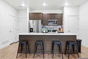 Kitchen with dark brown cabinetry, a center island with sink, tasteful backsplash, stainless steel appliances, and a breakfast bar