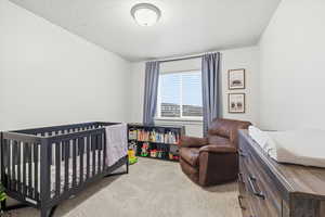 Bedroom with a nursery area, light carpet, and a textured ceiling