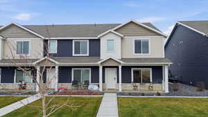 View of front of house with stone siding, roof with shingles, covered porch, a front yard, and board and batten siding