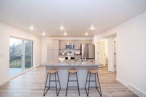 Kitchen with appliances with stainless steel finishes, a kitchen breakfast bar, an island with sink, light wood-type flooring, and recessed lighting