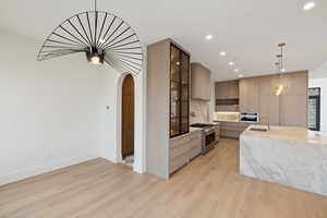 Kitchen with light stone countertops, arched walkways, pendant lighting, modern cabinets, and appliances with stainless steel finishes