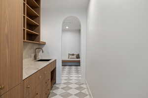 Butlers Pantry  with light flooring, arched walkways, brown cabinetry, open shelves, and light stone counters