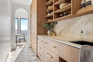 Kitchen featuring arched walkways, light wood finish cabinets, backsplash, open shelves, and light stone countertops