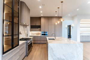 Kitchen with light stone counters, hanging light fixtures, stainless steel appliances, arched walkways, and recessed lighting