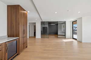 Basement Kitchen bar  featuring brown cabinetry, modern cabinets, wine cooler, recessed lighting, and light wood-style floors