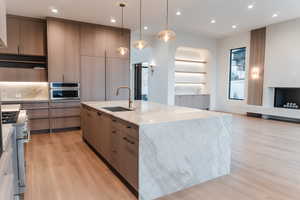 Kitchen with built in features, a center island with sink, pendant lighting, light stone counters, and recessed lighting