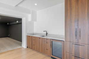 Kitchen wet bar featuring modern cabinets, wine cooler, brown cabinetry, light stone countertops, and light wood-type flooring