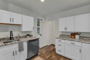 Kitchen featuring white cabinetry, dishwasher, light stone counters, and dark wood-type flooring