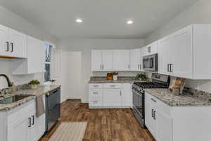 Kitchen with stainless steel appliances, light stone counters, white cabinets, dark wood-type flooring, and recessed lighting