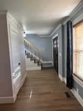Foyer entrance with stairs, dark wood-style flooring, and ornamental molding