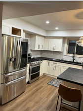 Newly remodeled kitchen featuring stainless steel appliances, white cabinets, new flooring, custom backsplash, and recessed lighting.
