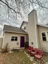 Back of house with a shingled roof, a chimney, and entry steps