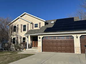 View of front facade with stucco siding, roof with shingles, and stone siding