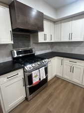 Kitchen with range, custom wall chimney exhaust hood, white cabinetry, and tasteful backsplash