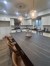 Kitchen featuring white cabinets, hanging light fixtures, a breakfast bar area, decorative backsplash, and recessed lighting.