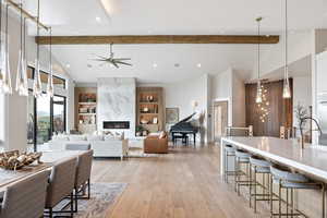 Dining space with a chandelier, beamed ceiling, a premium fireplace, light wood-style floors, and built in shelves