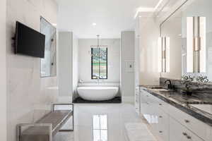 Full bathroom featuring a soaking tub, double vanity, light marble finish flooring, recessed lighting, and tile walls