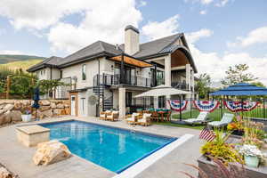 Back of house featuring a balcony, a patio, stucco siding, stairs, and a chimney