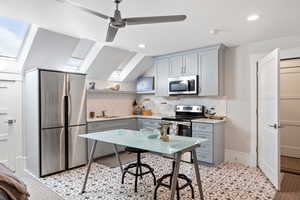 Kitchen with gray cabinetry, stainless steel appliances, a skylight, decorative backsplash, and a ceiling fan