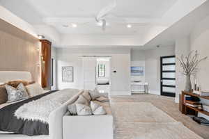 Carpeted bedroom featuring a barn door, ceiling fan, ensuite bath, recessed lighting, and a raised ceiling
