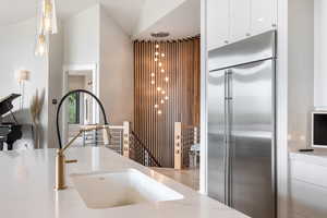 Kitchen featuring stainless steel built in refrigerator, white cabinets, decorative light fixtures, and light stone countertops