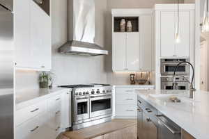 Kitchen featuring wall chimney range hood, appliances with stainless steel finishes, and white cabinets