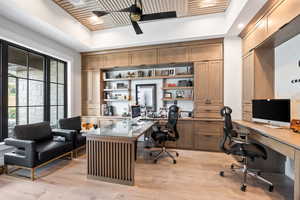 Home office with built in study area, light wood finished floors, a ceiling fan, and a raised ceiling